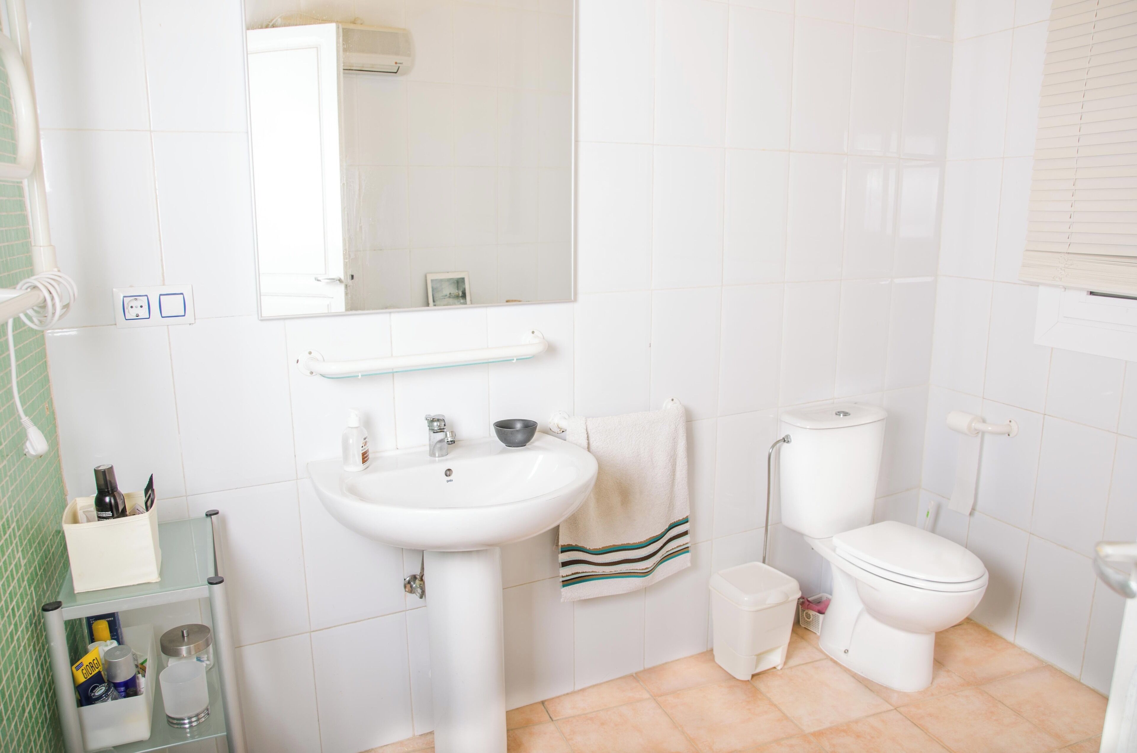 A bathroom with a white sink, toilet, and mirror. There is a towel rack with a towel hanging on it. A small trash bin is next to the toilet.