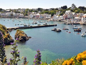 Uma cidade costeira com um porto cheio de barcos, rodeada por edifícios coloridos e vegetação.