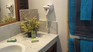 Een badkamer met een marmeren wastafel, een spiegel, een handdoekhouder met blauwe handdoeken, een potplant en een decoratief wandpaneel.