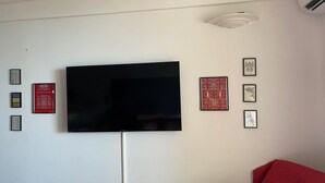 Een woonkamer met een flatscreen televisie aan de muur, omringd door ingelijste kunstwerken en een rode bank.