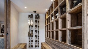 A hallway with wooden shelves on the right, displaying various items. There are benches on the left and a wall-mounted shoe rack in the center. - Spacious chalet with Nordic bath and steam room in Saint-Martin-de-Belleville (Saint-Martin-de-Belleville)