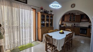 Uma sala de jantar com mesa posta para quatro pessoas, um armário de madeira com portas de vidro e uma cozinha ao fundo.