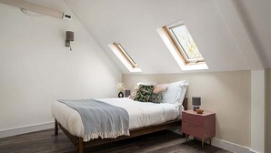 Een slaapkamer met een schuine kap, een bed met houten frame, een nachtkastje en twee dakramen.