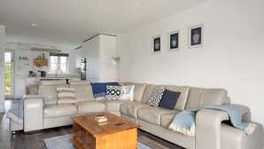 Een moderne woonkamer met een beige modulaire bank, een houten salontafel en een keuken op de achtergrond.