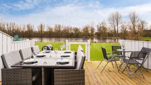 Een terras met eettafel voor vier personen, omringd door rieten stoelen, met uitzicht op een meer.