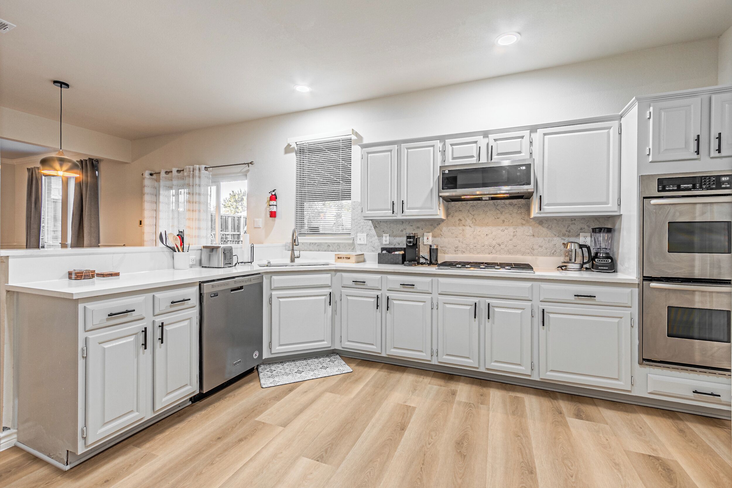 A modern kitchen with white cabinetry, stainless steel appliances, and a wooden floor.