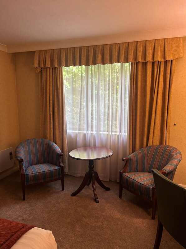 A room with two striped armchairs, a round table, and a window with curtains. - Urban Hotel Grantham (Grantham)