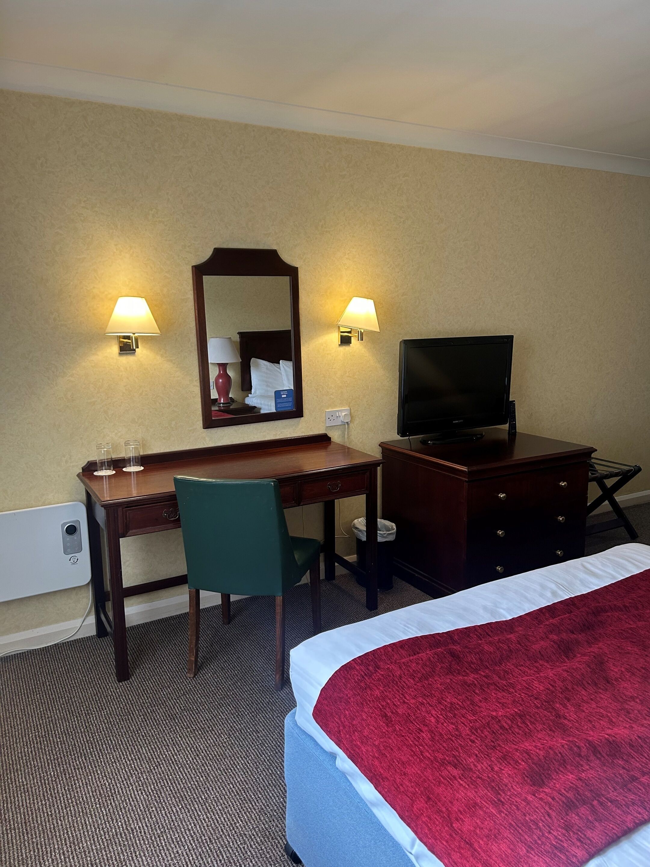 Une chambre d’hôtel équipée d’un lit, d’un bureau, d’une chaise, d’une télévision et de deux lampes fixées au mur.