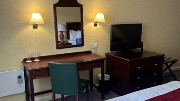 Une chambre d’hôtel équipée d’un lit, d’un bureau, d’une chaise, d’une télévision et de deux lampes fixées au mur.