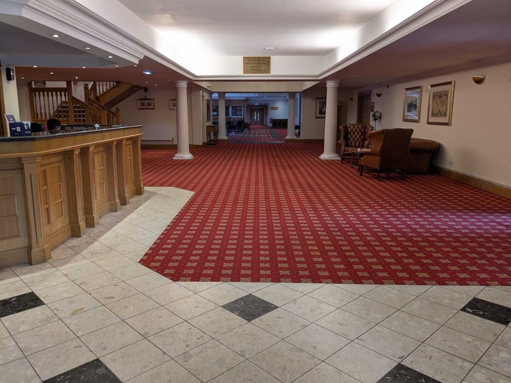 A hotel lobby with a red carpet, a reception desk, and a staircase.