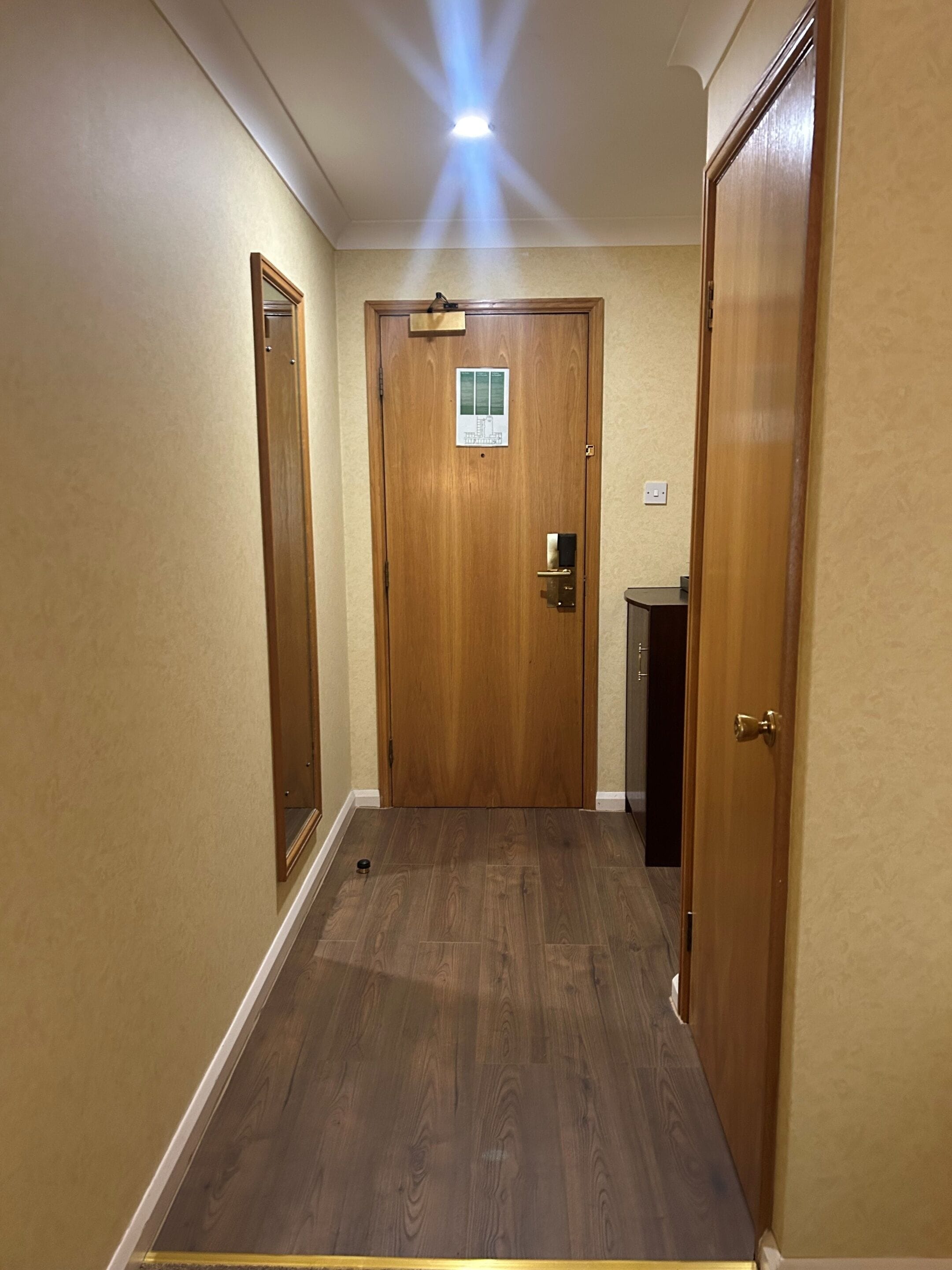 A hallway with wooden doors, a light fixture, and a small sign on the door.