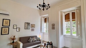 A living room with a sofa, a dining table with chairs, a chandelier, and framed pictures on the wall. - La Piattaforma, your home with a private sea view (Santa Cesarea Terme)