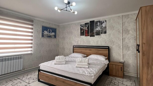 A bedroom with a bed, a bedside table, a wardrobe, a radiator, and a window with blinds.