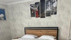 A neatly made bed with white linens and towels, a wooden headboard, a patterned rug, and a small wooden nightstand with a lamp.