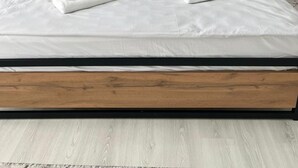 A neatly made bed with white linens and towels, a wooden headboard, and a wall with a patterned wallpaper and a framed artwork above it.