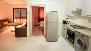 Una cocina moderna con refrigerador, estufa y lavadora. Hay un comedor con mesa y sillas, y una sala de estar con sofá y televisor.