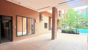 Un patio interior con suelo de baldosas, un acceso por puerta de vidrio y vistas a una piscina y vegetación al exterior.