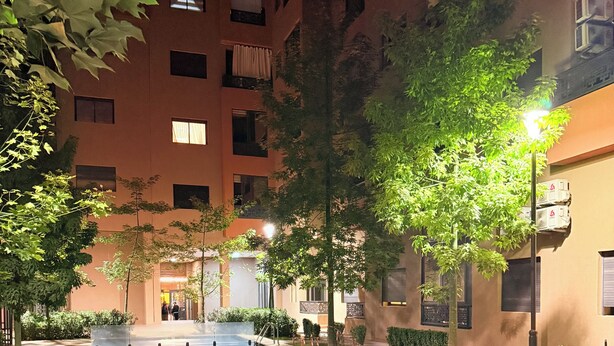Una piscina rodeada de jardines con árboles y un edificio al fondo.
