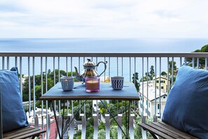 Un balcon avec une table dressée pour deux personnes, offrant une vue sur la côte.
