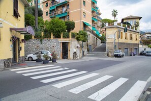 A street view with a crosswalk, parked cars, and buildings with balconies and plants.