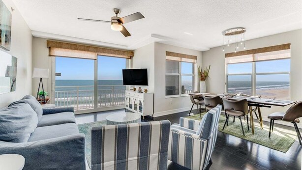 A modern living room with a large sofa, striped armchairs, a dining area, and a TV.