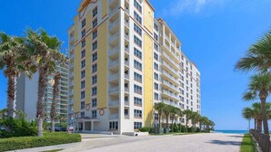 A multi-story hotel with balconies, palm trees, and a clear blue sky.