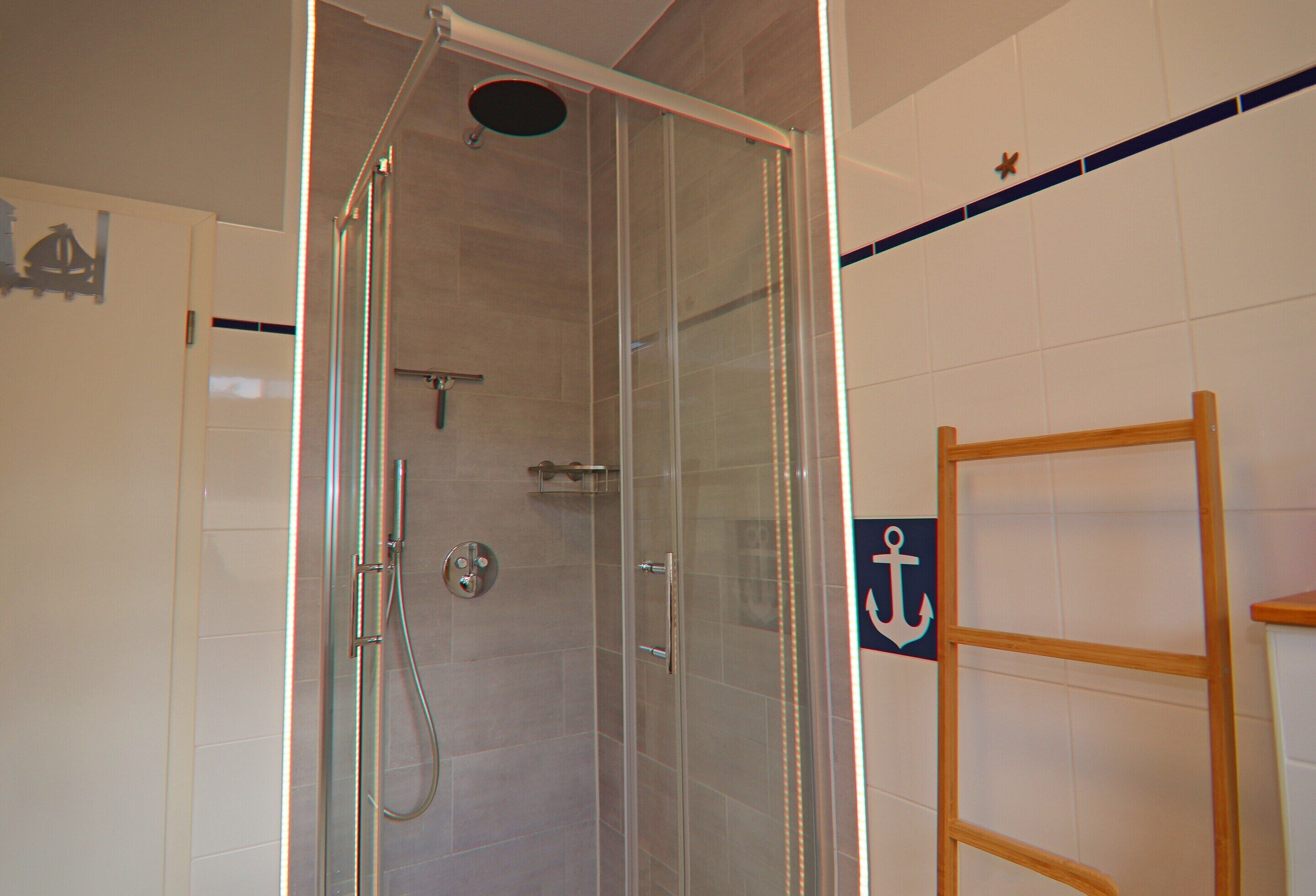 A glass-enclosed shower with a handheld showerhead and a handheld faucet.