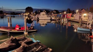 A marina at dusk with boats docked, a small boat with a red cover, and a building with a sign. - Stylish Ground-floor Stay (Timmendorfer Strand)
