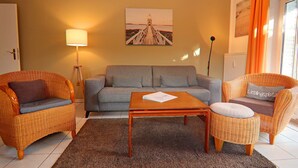 A living room with wicker furniture, a grey sofa, a wooden coffee table, and a lamp. - Stylish Ground-floor Stay (Timmendorfer Strand)