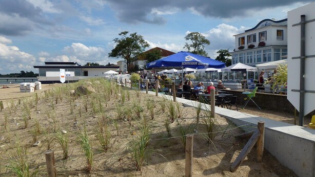A beachside restaurant with outdoor seating and a blue umbrella. - Stylish Ground-floor Stay (Timmendorfer Strand)