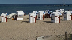 Beach huts with numbers, a sandy beach, and a pier in the background. - Stylish Ground-floor Stay (Timmendorfer Strand)