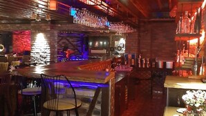 Un espace bar avec un plafond en bois, des tabourets de bar et un comptoir où sont exposées des bouteilles.