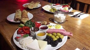 Une table dressée dans un restaurant, avec divers plats, notamment du fromage, des olives et de la charcuterie, et un panneau lumineux au néon en arrière-plan.