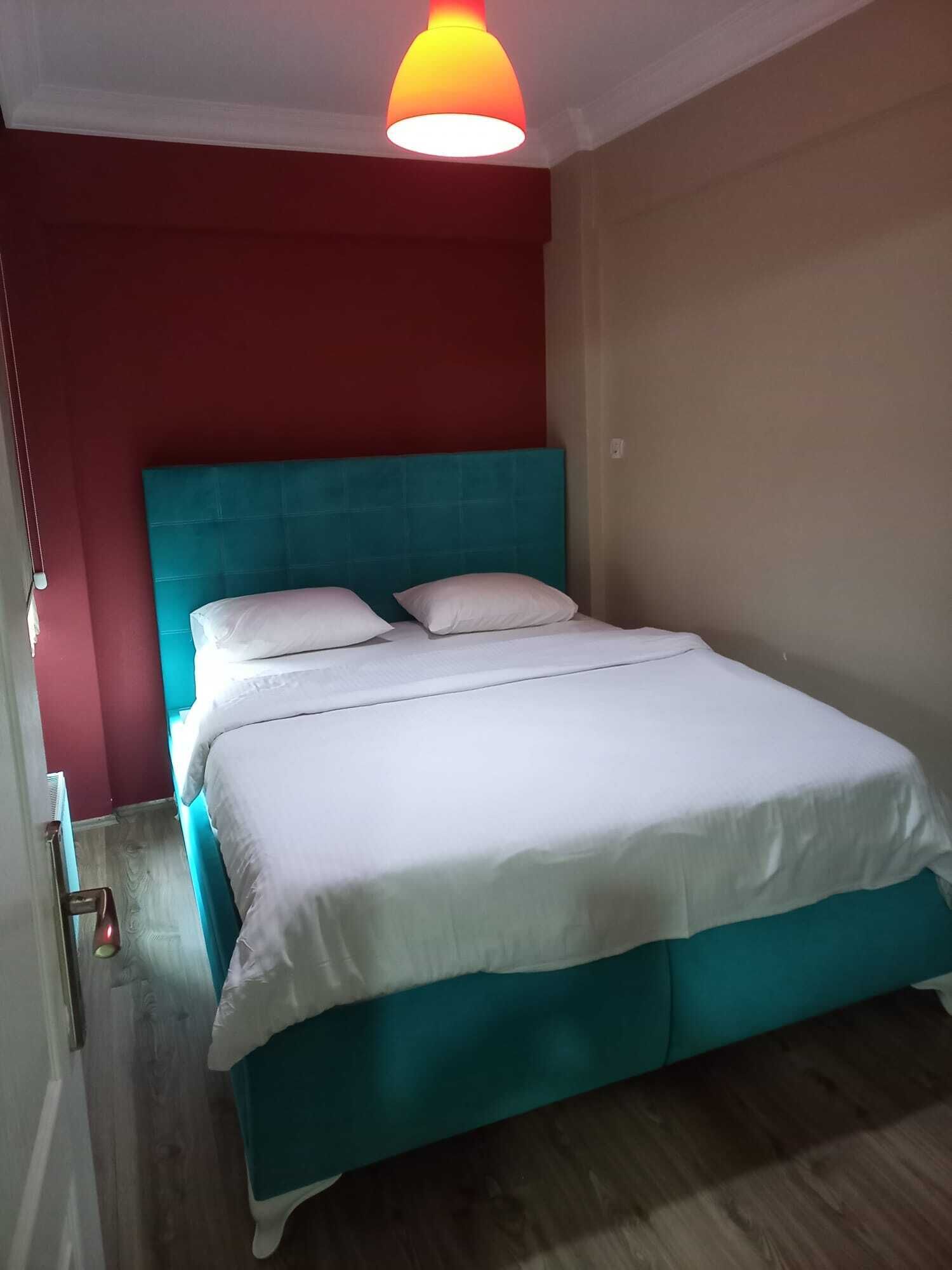 Un dormitorio con cabecera color turquesa, ropa de cama blanca y una pared de acento roja.