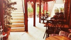 Un espace extérieur aménagé en terrasse, avec des tables et des chaises en bois, des plantes en pot et un sol à motifs.