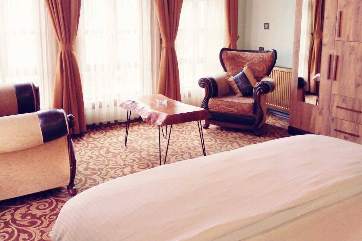 Hotellihuone, jossa on suuri sänky, puinen vaatekaappi, tuoli ja pieni pöytä.