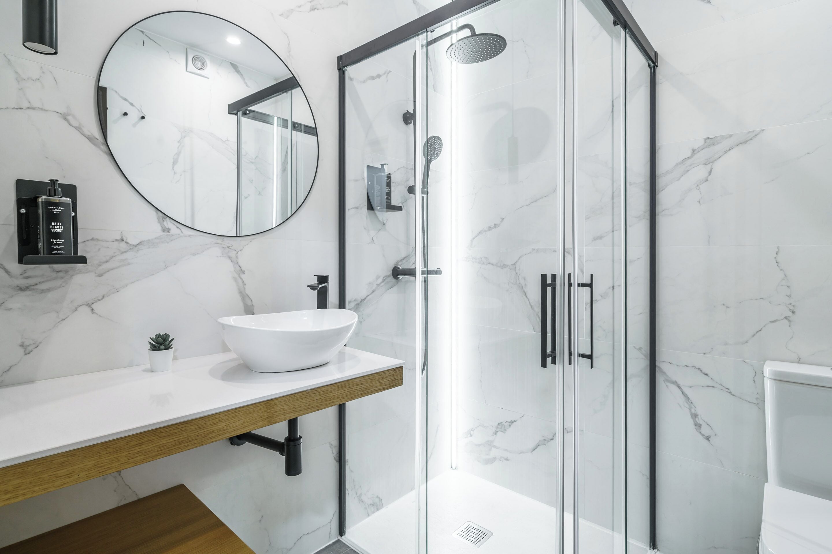 A modern bathroom with a white marble sink, a round mirror, and a glass-enclosed shower.