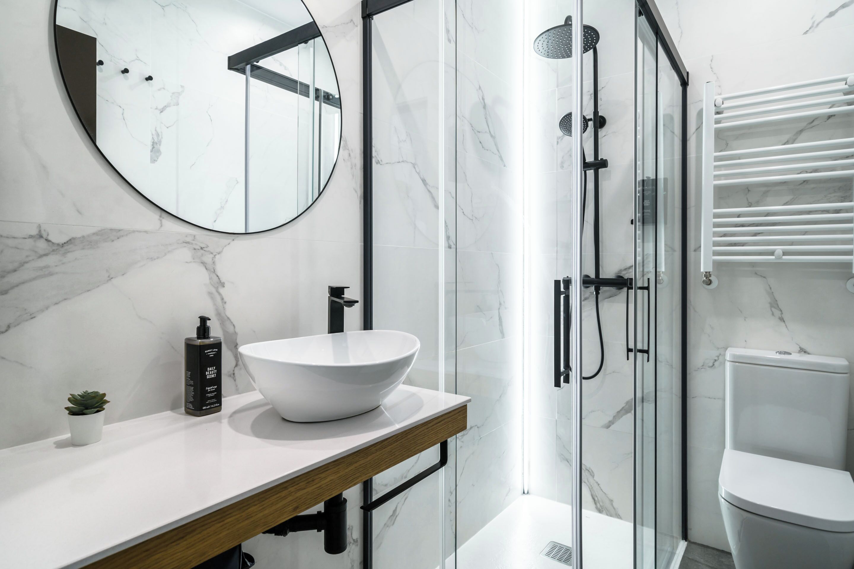 A modern bathroom with a white marble sink, a round mirror, and a glass shower enclosure.