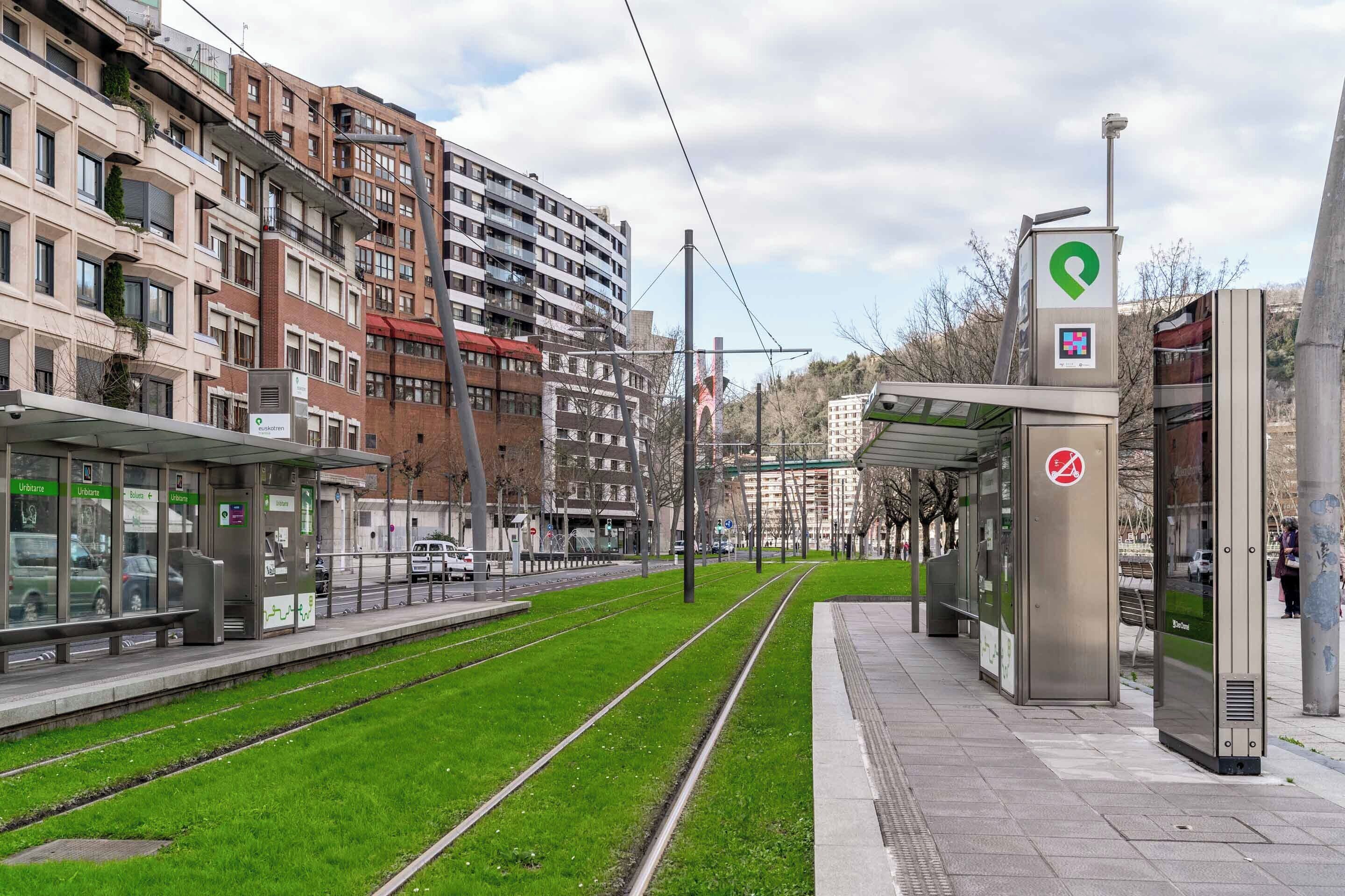 A tram station with a covered waiting area, a ticket machine, and a pedestrian path alongside the tracks.
