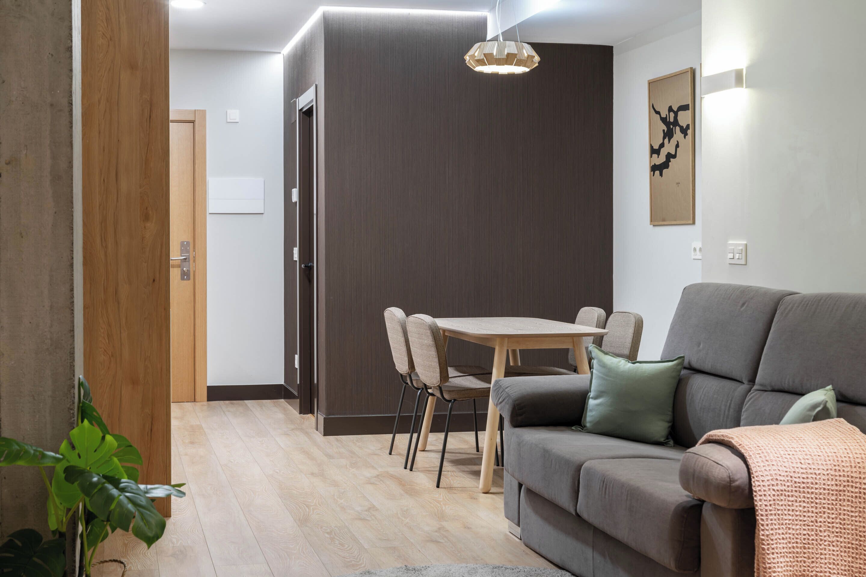 A modern living room with a sofa, a dining table with chairs, and a wooden door.