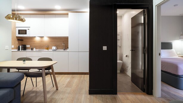 A modern kitchen with white cabinets, a microwave, and a dining area with a table and chairs. - Limehome Bilbao Tristan de Leguizamon (Bilbao)