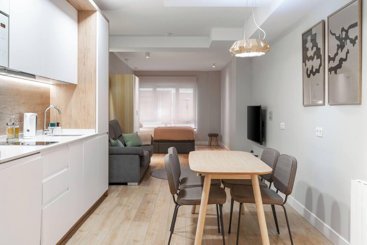 Una cocina moderna con armarios blancos, encimera de madera y un comedor con mesa y sillas.