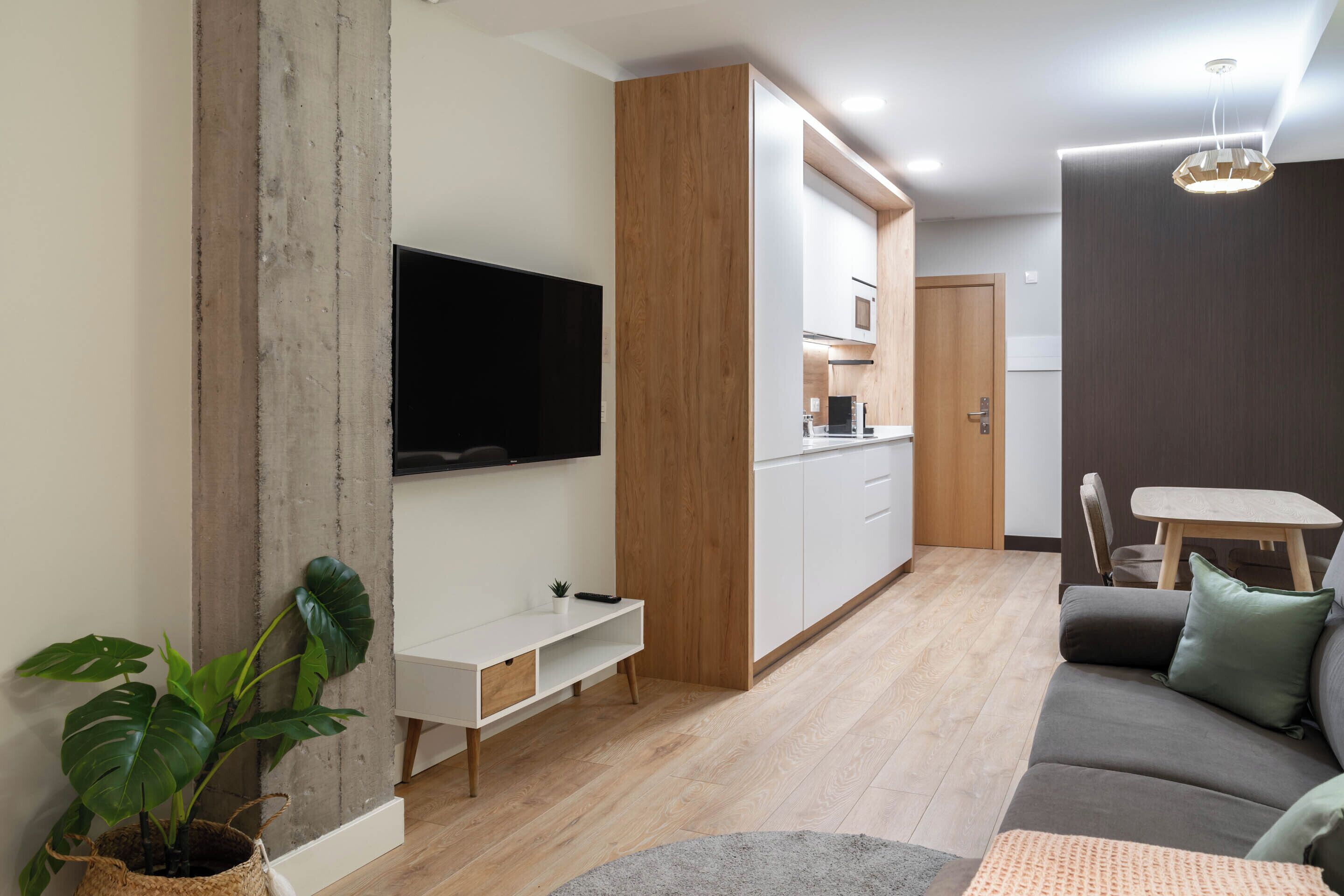A modern living room with a flat-screen TV, a sofa, a coffee table, and a dining area with a table and chairs.