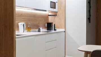 Una cocina moderna con armarios blancos, microondas, cafetera y fregadero.