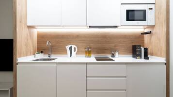 Una cocina moderna con armarios blancos, microondas integrado, hervidor de agua y cafetera.