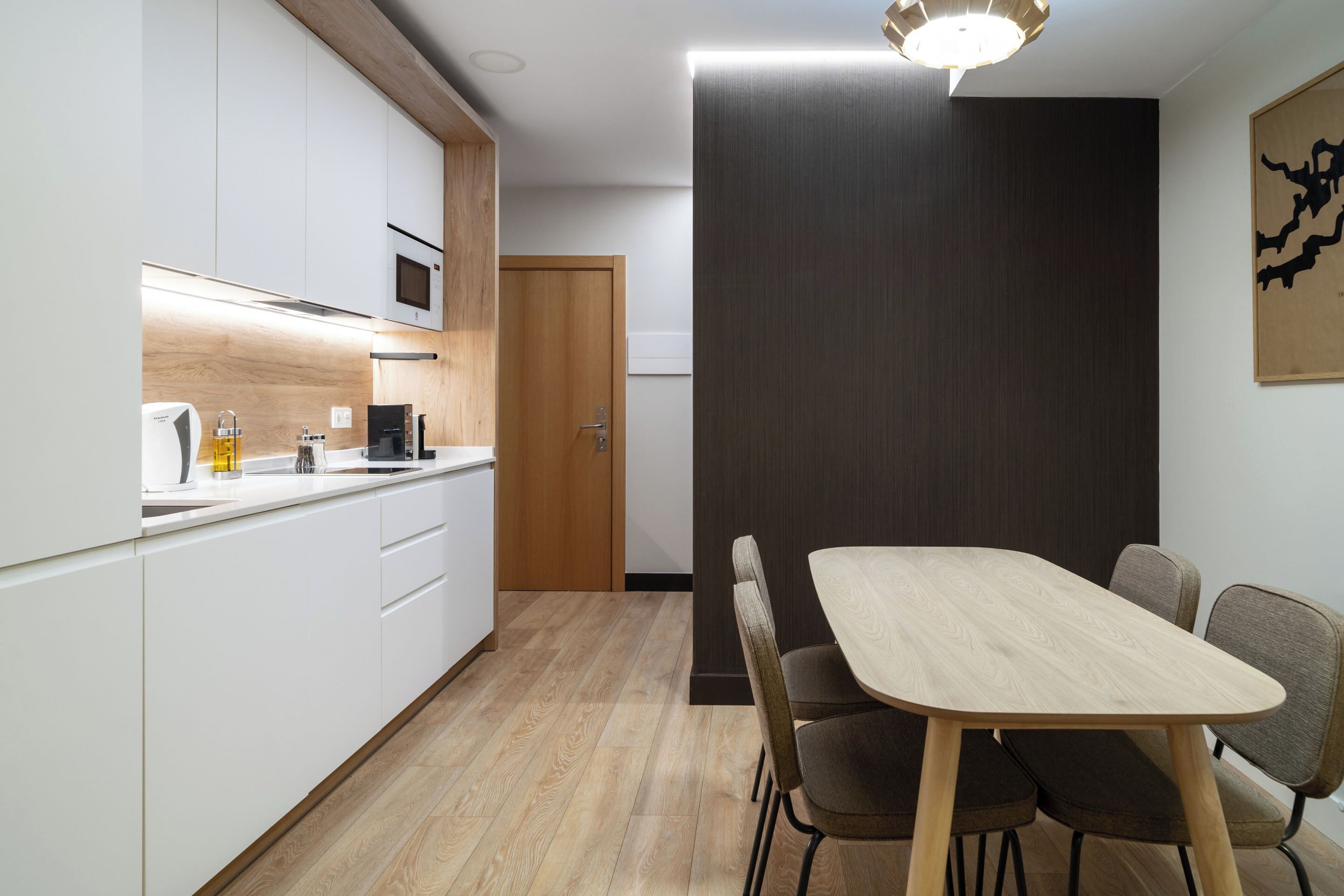 A modern kitchen with white cabinets, a wooden countertop, and a dining area with a wooden table and chairs.