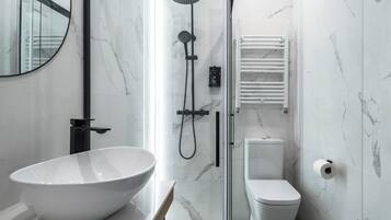 Un baño moderno con un lavamanos blanco de diseño, una ducha con cerramiento de vidrio y un inodoro blanco.