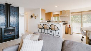 A modern living room with a gray sofa, a fireplace, and a kitchen area with a bar and seating. - Private Blufftop · Oceanview Hot Tub · Fire Pit (Port Angeles)
