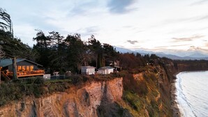A coastal cliffside property with multiple cabins and a large house, featuring a scenic ocean view and mountainous backdrop. - Private Blufftop · Oceanview Hot Tub · Fire Pit (Port Angeles)