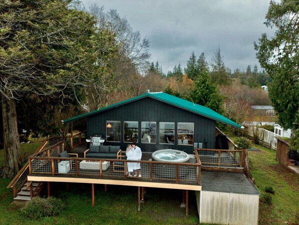 A cabin with a deck, outdoor seating, and a hot tub.